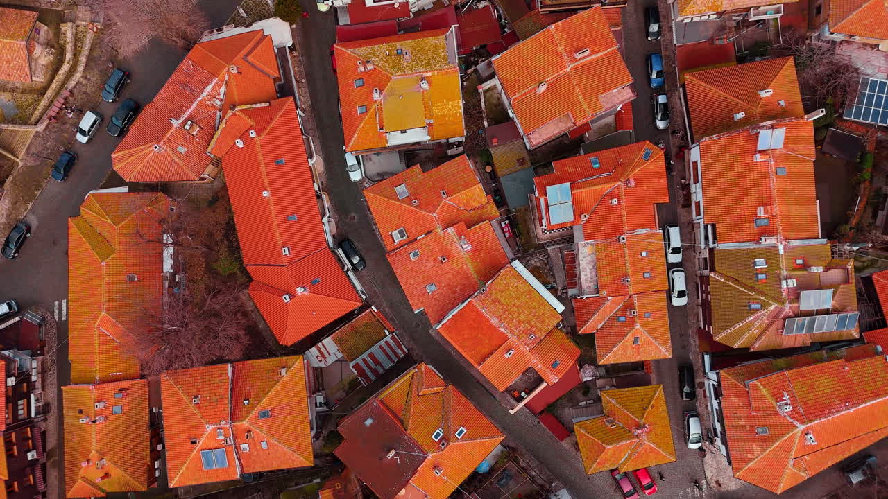 Top down aerial view of red tile rooftops in old town. Orange clay tile roofs, narrow streets, and parked cars in a historic European district