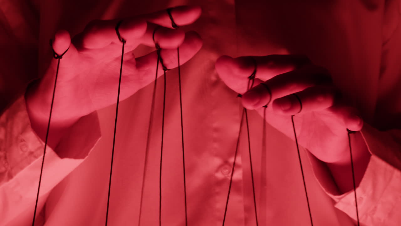 Close-Up of Hands Manipulating Puppet Strings with Red Lighting