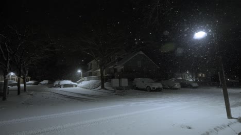 snow capped neighborhood at night, cold winter weather, snow covered streets and cars, houses, lamp, static shot, copy space, dark sky