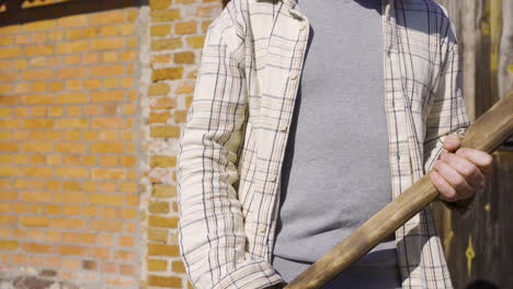 Close-up-view-of-a-man-in-plaid-shirt-holding-an-ax-outside-a-country-house