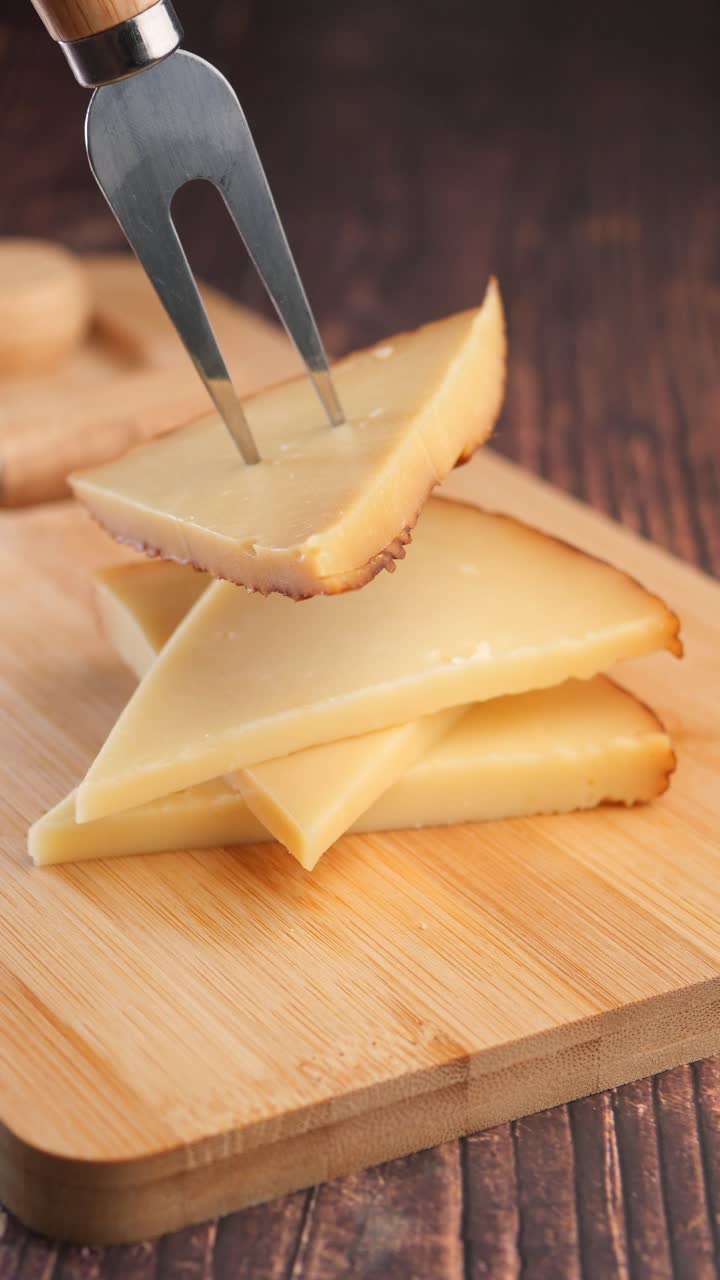 Pegando uma fatia de queijo com um garfo de uma tábua de madeira
