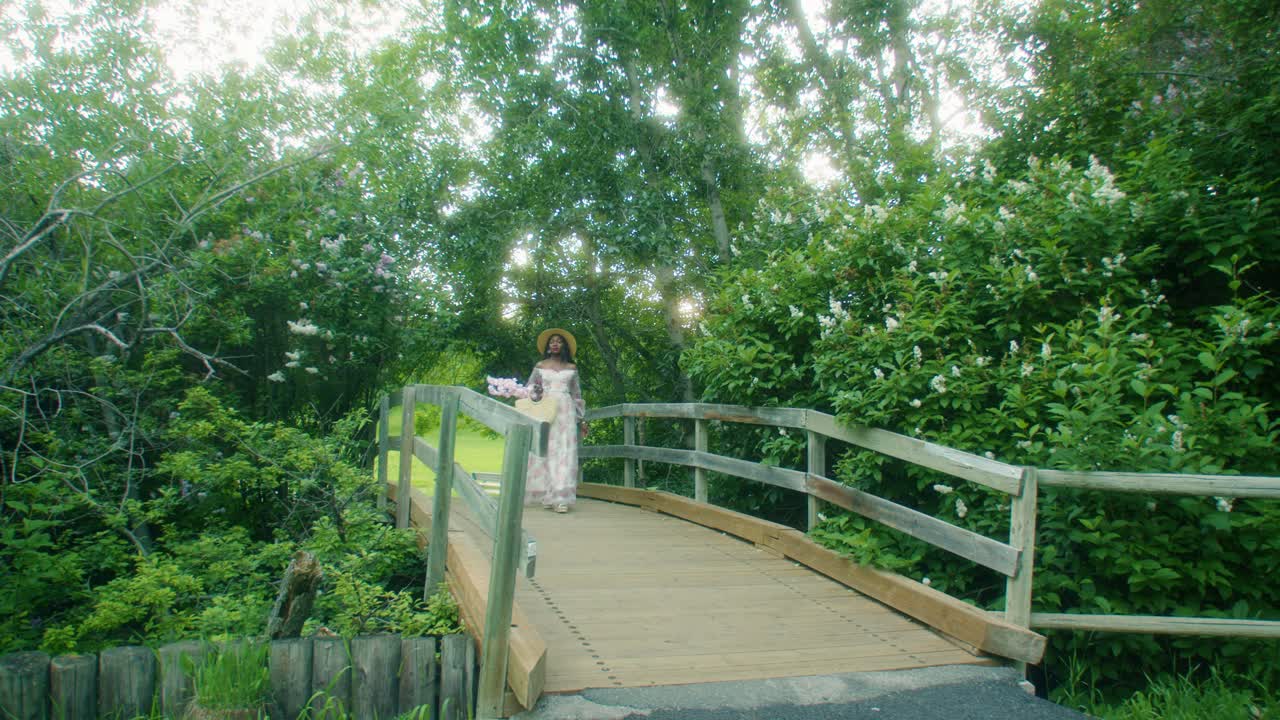 mujer negra con cesta de picnic caminando sobre el puente oliendo flores lilas ancho pan ancho