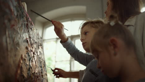 geïnspireerde familie die samen tekent in de studio. vrouwelijke leraar die penseelstreken maakt.