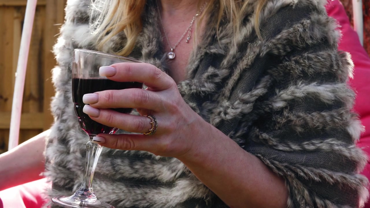 Donna attraente si gode un bicchiere di vino su un'altalena da giardino, primo piano con zoom e slow motion