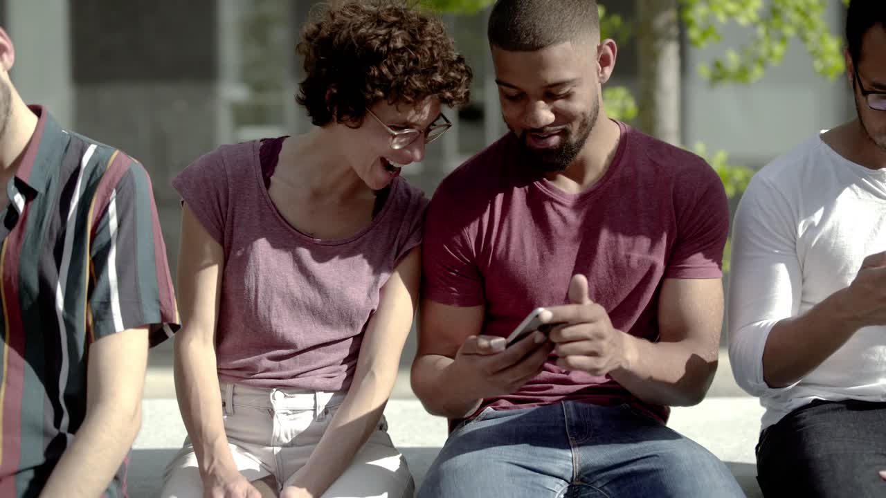 vista frontal de dos amigos sentados y mirando el teléfono inteligente
