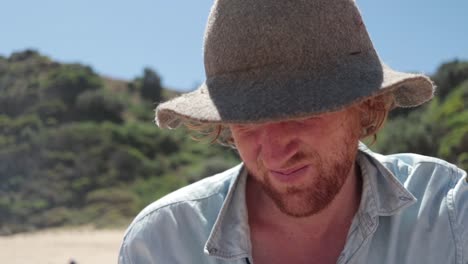 una toma en cámara lenta de un hombre pelirrojo mirando hacia arriba de un libro mientras lee en la playa