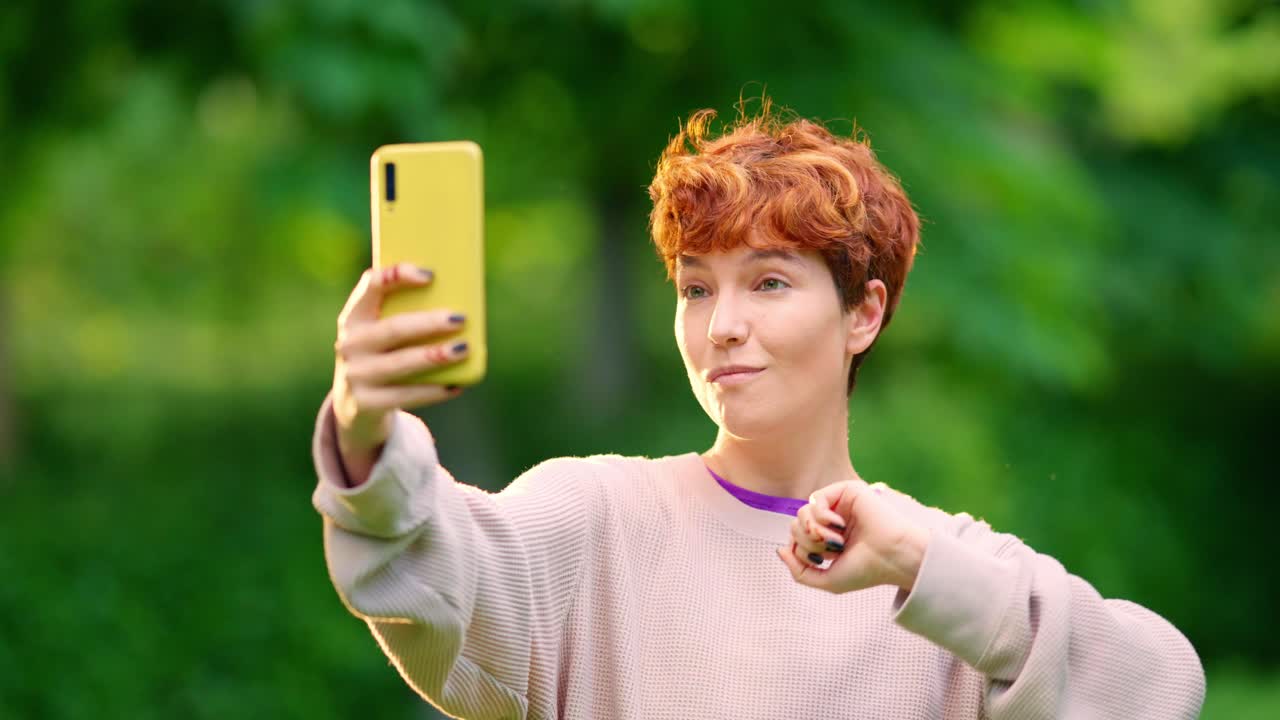 Young woman taking a selfie with her phone in a park