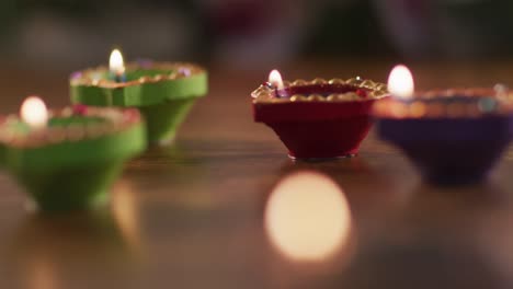 four lit candles in decorative clay pots on wooden table top, bokeh flame in foreground