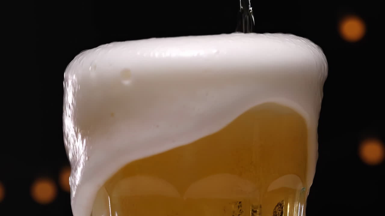 Bira sıçraması - lambalarla karanlık bir arka planda bir bardağa dökülen şarap, şampanya, bira; köpük kabarcıkları yükseliyor ve taşıyor, siyah bir arka planda ferahlatıcı bir sıçrama.