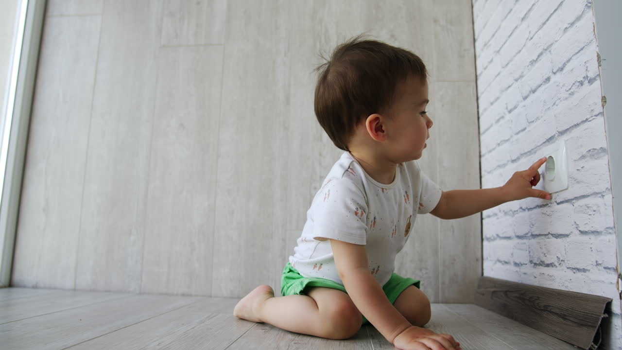 Little toddler boy having fun time at home. Kid sits on the floor and then crawls to the electric socket on the wall.