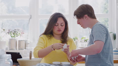 Una-Pareja-Joven-Con-Síndrome-De-Down-Poniendo-Cajas-De-Pastel-De-Papel-En-Una-Bandeja-En-La-Cocina-De-Casa