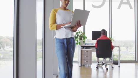 African-american-creative-businesswoman-standing-with-laptop-in-modern-interiors