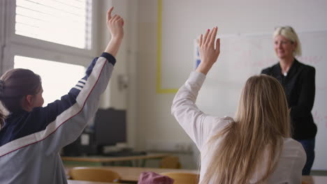 Two-girl-students-during-a-lecture,-raise-hands-and-answer-a-question,-rear-view