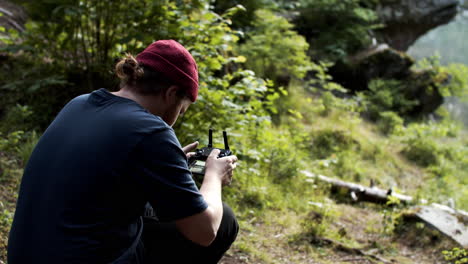 fotógrafo revisando los controles de drones mientras está sentado en el bosque - plano medio