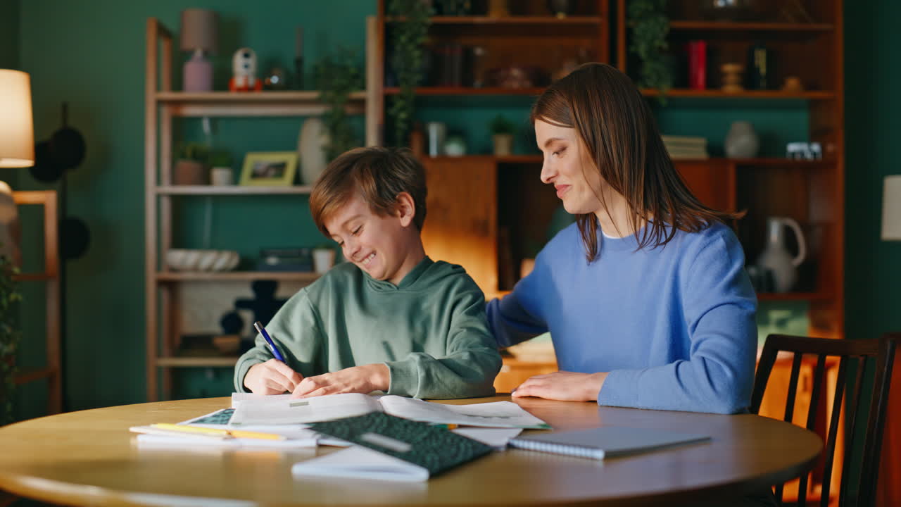 Glad mor og sønn driver hjemmeundervisning sammen, nærbilde. Kvinne som støtter skolegutten.