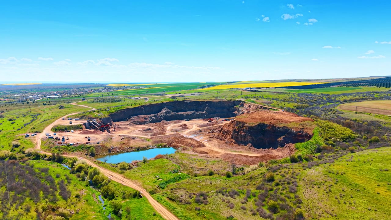 Pedreira industrial a céu aberto e vista aérea de fazenda solar distante. Ampla vista aérea de uma pedreira de pedra com um lago azul cercado por paisagem verde e uma fazenda solar distante.