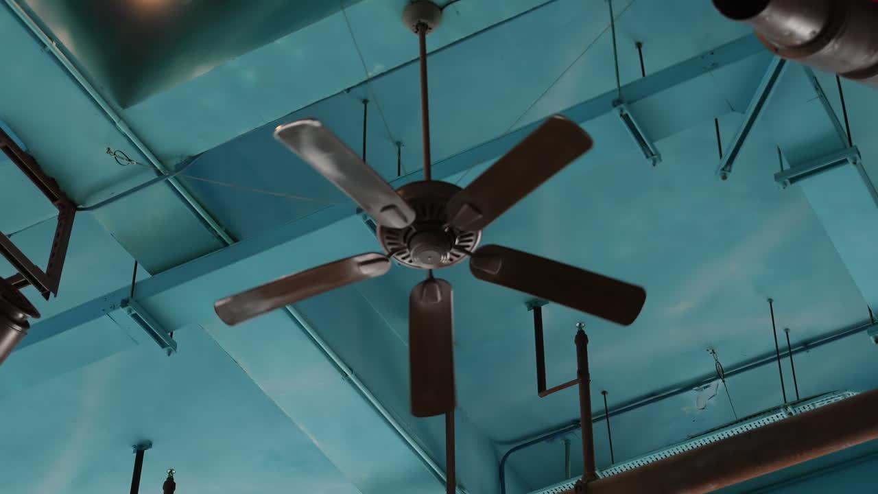 Ventiladores de teto e canos contra um teto industrial azul claro