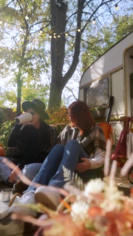 two women enjoying a cozy autumn day by a trailer