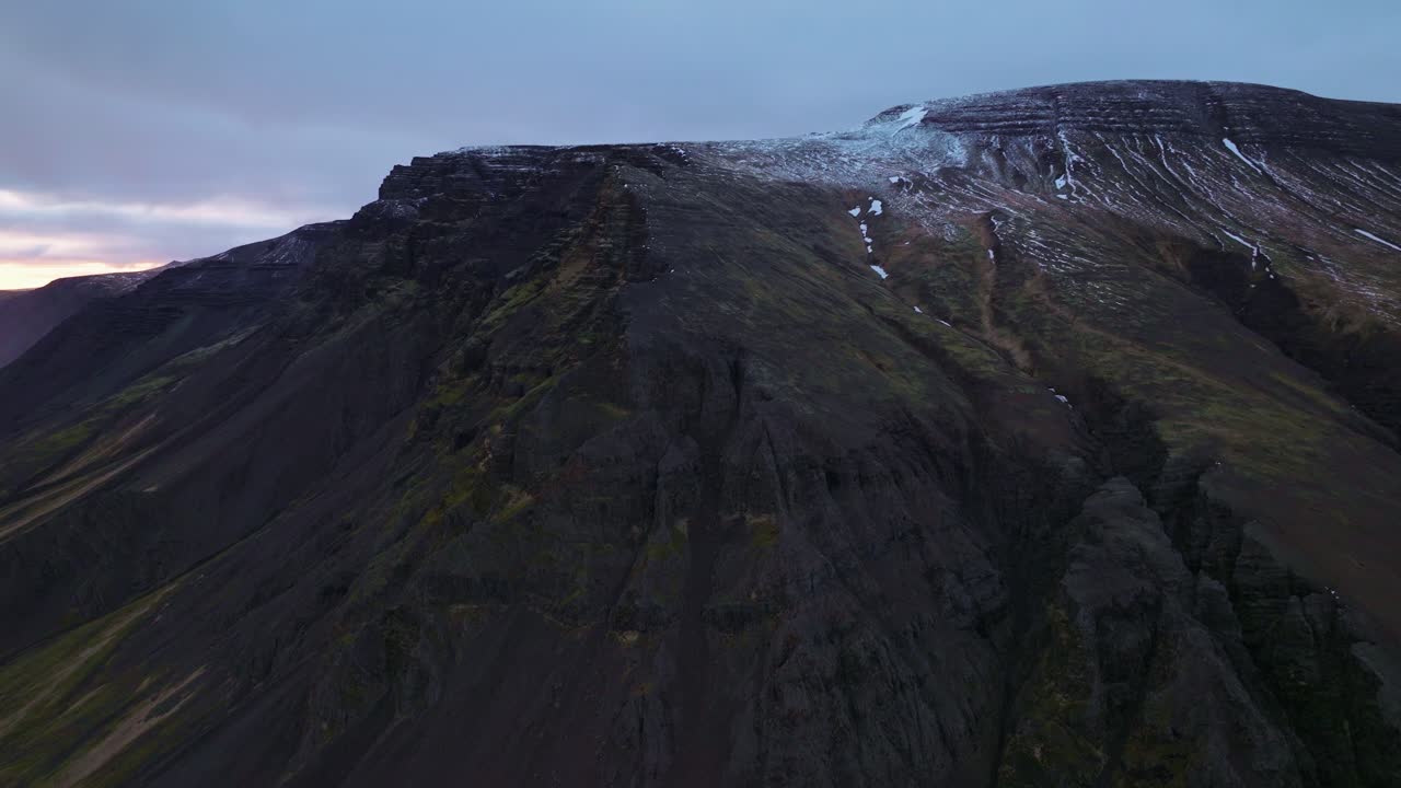 fotografía aérea de una montaña escarpada en akranes, islandia, capturada al anochecer con un cielo dramático y manchas de nieve en la cumbre