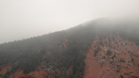 Aerial-approach-towards-forested-ridge-covered-in-mist-Cheyenne-Valley,-Colorado
