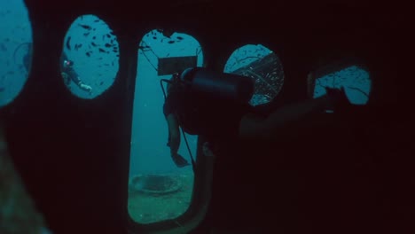 scuba divers explore sunken shipwreck portholes