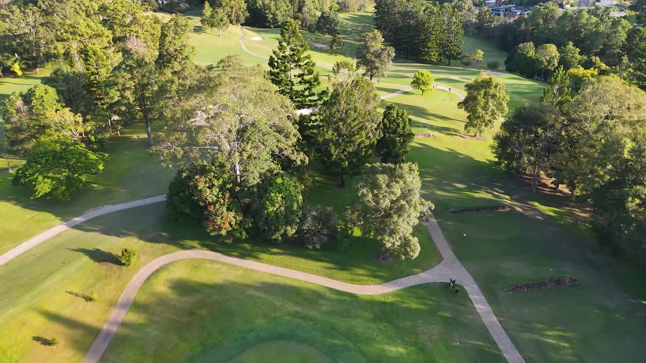Drone captures lush golf course with fairways, bunkers, and trees in bright daylight