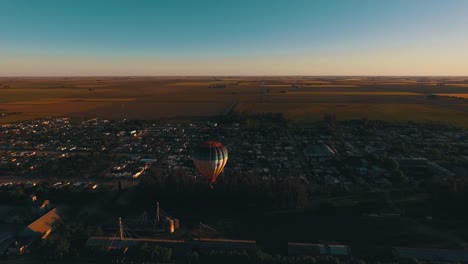 drone shot of a hot air balloon floating over a small city with a paraglide in the background