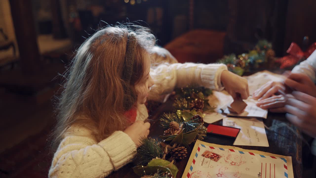Little girl puts seal on envelopes at Christmas. Children help elves to prepare letters for other kids from santa Claus. A lot of letters with wishes and envelopes on the table.