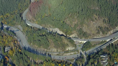 Vista-Aérea-De-La-Autopista-Con-Tráfico-En-Una-Zona-Boscosa-Montañosa-Y-Soleada.