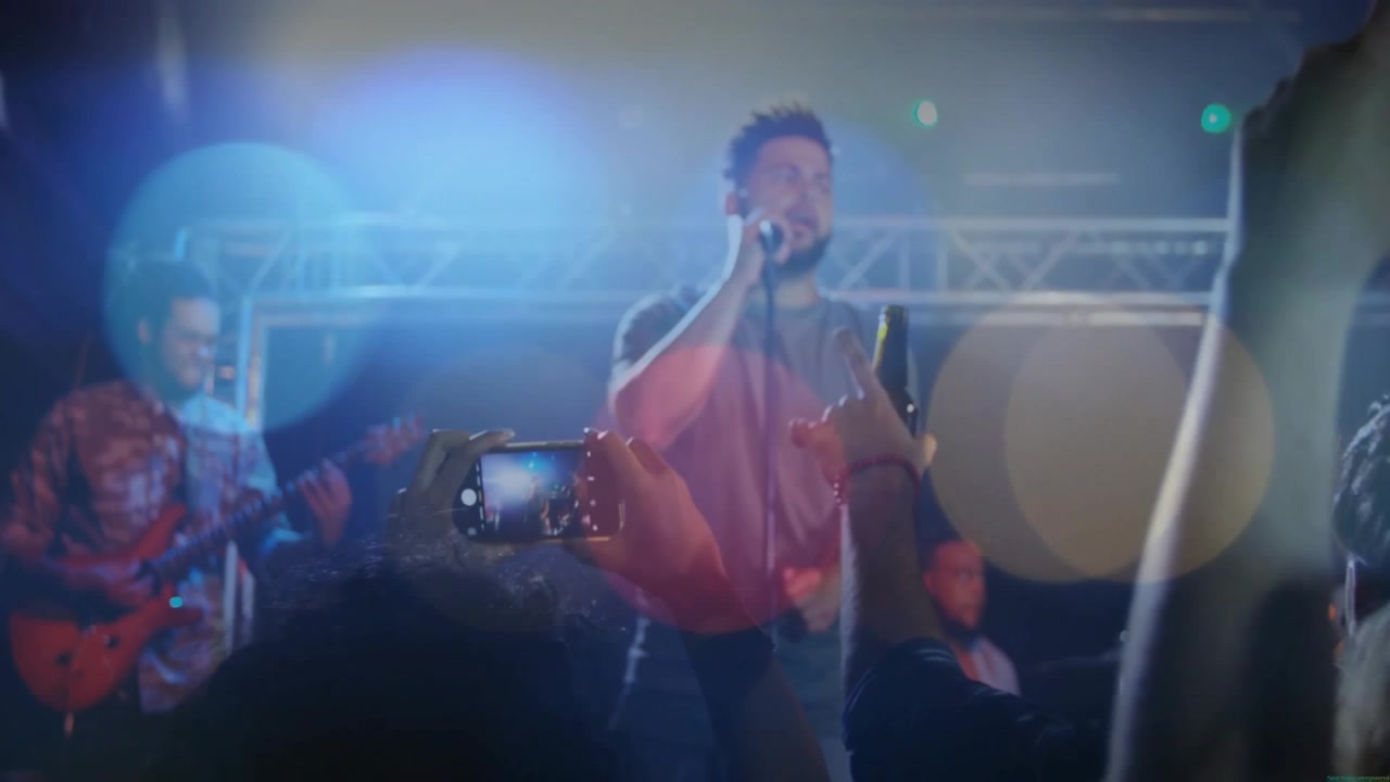 Lead vocalist starting song at music stage mic, audience raising phones to record, creating flares