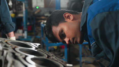 mechanic working diligently on engine block in automotive workshop, focusing on detailed repair and inspection, with partial view of observer hand in white glove in mechanical shop