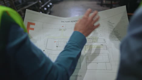Unrecognisable supervisors holding paper project professional factory plan.