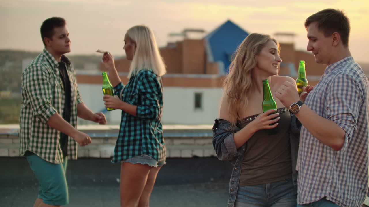Two young couples in love are dancing on the roof and eating pizza with beer on the party. They enjoy moments with their soul mates.