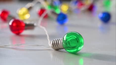 visto en primer plano contra una superficie blanca, una agrupación de luces de navidad muestra un claro enfoque en una bombilla verde, con bombillas azules, rojas, amarillas y verdes sirviendo como fondo