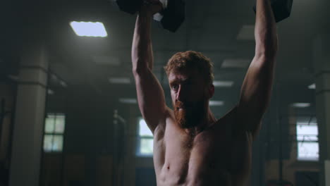 portrait of a man pushing dumbbells over his head in the gym. training of endurance and arm and shoulder muscles