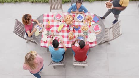 Diverse-man-and-woman-serving-food-to-friends-at-dinner-table-in-garden,-slow-motion