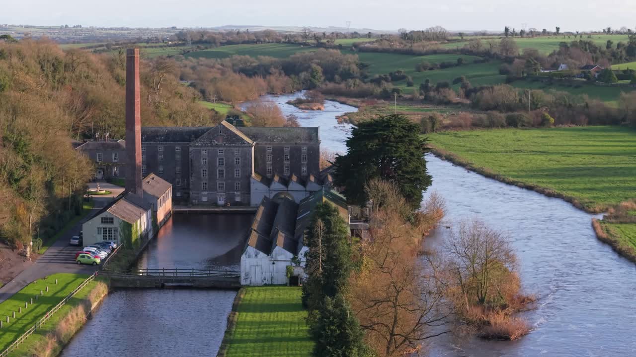 Historic Georgian manor with a red brick chimney beside a tranquil river and green fields in Ireland