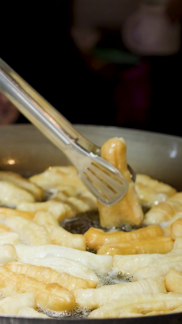 Primo piano di mani che usano pinze di metallo per girare pasta fritta dorata nell'olio bollente.