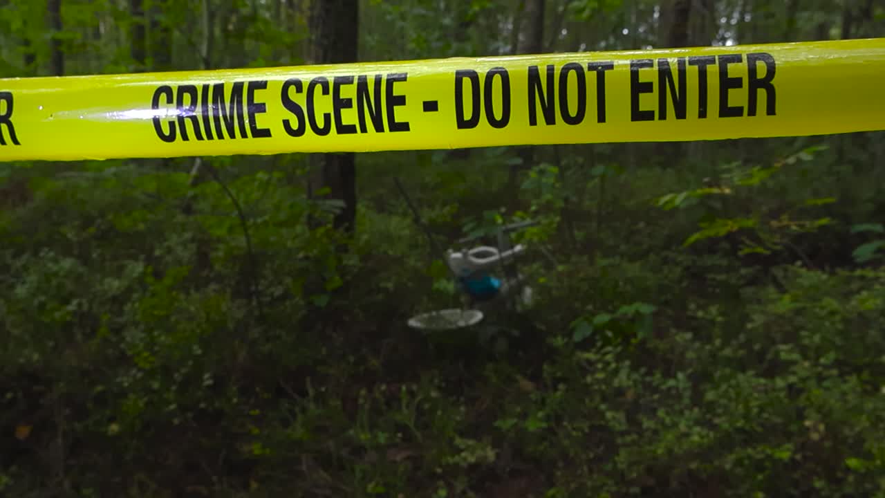 Eerie video of a children bicycle left behind by a criminal while a yellow coloreed police crime scene forensic investigation tape ribbon hangs in front of the scene. Foliage and dense thick forest