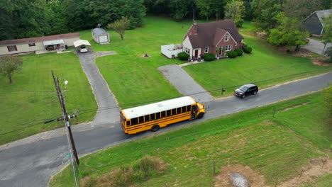 aerial top view of yellow american school bus stopping on road of suburb neighborhood. single family house with garden in pa,america. orbit view.