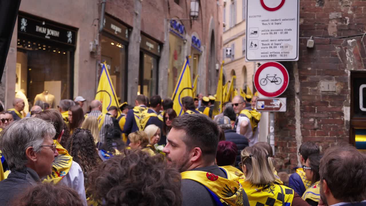 A large crowd of people marching down a narrow street during a parade or festival in Italy