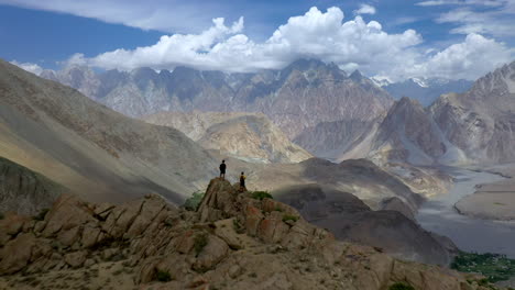 two people standing on peak at passu cones pakistan, cinematic wide revealing aerial shot