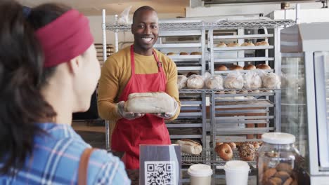 Diverse-worker-and-customer-offering-fresh-bread-in-bakery-in-slow-motion