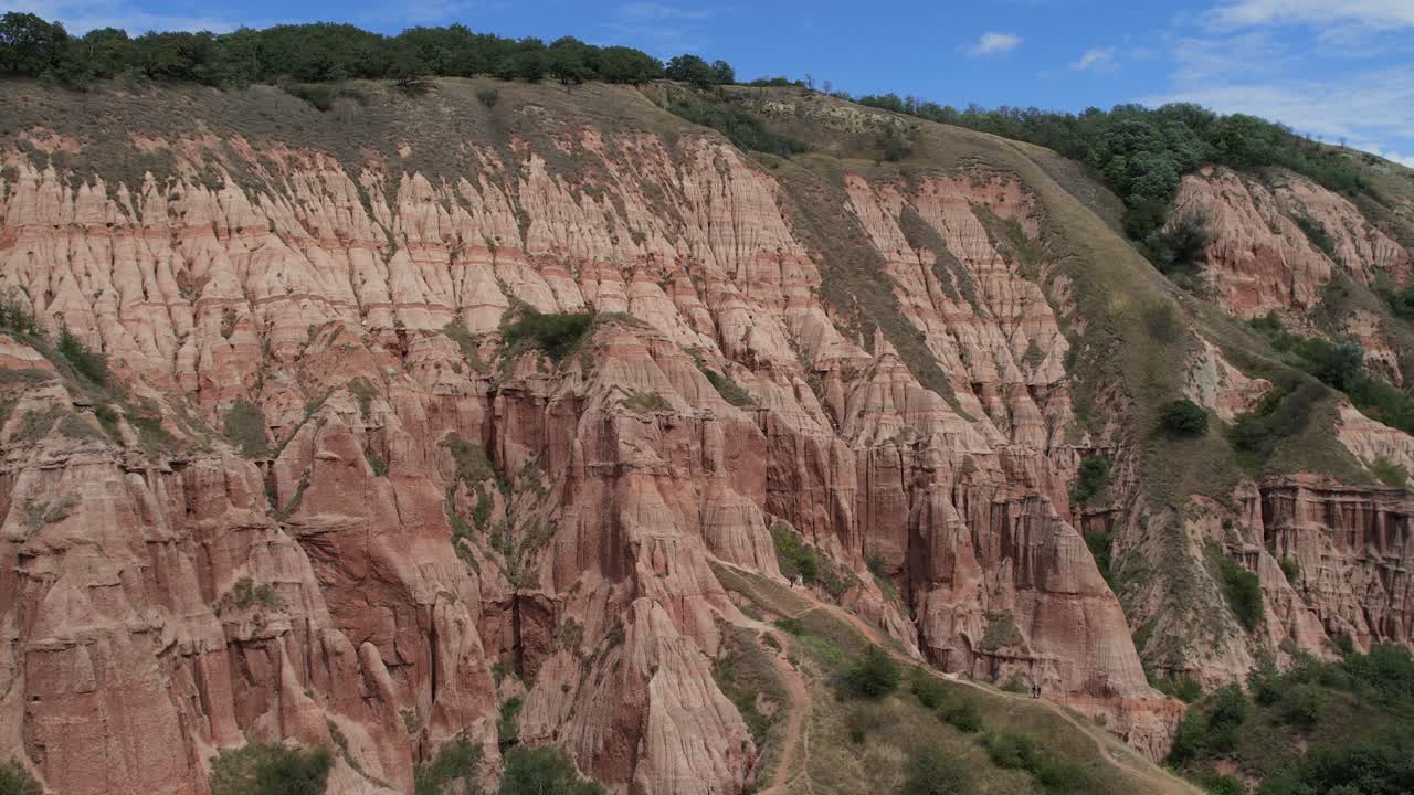 Wide panoramic slider shot over Rapa Rosie, revealing its towering red cliffs and dramatic textures under natural daylight.