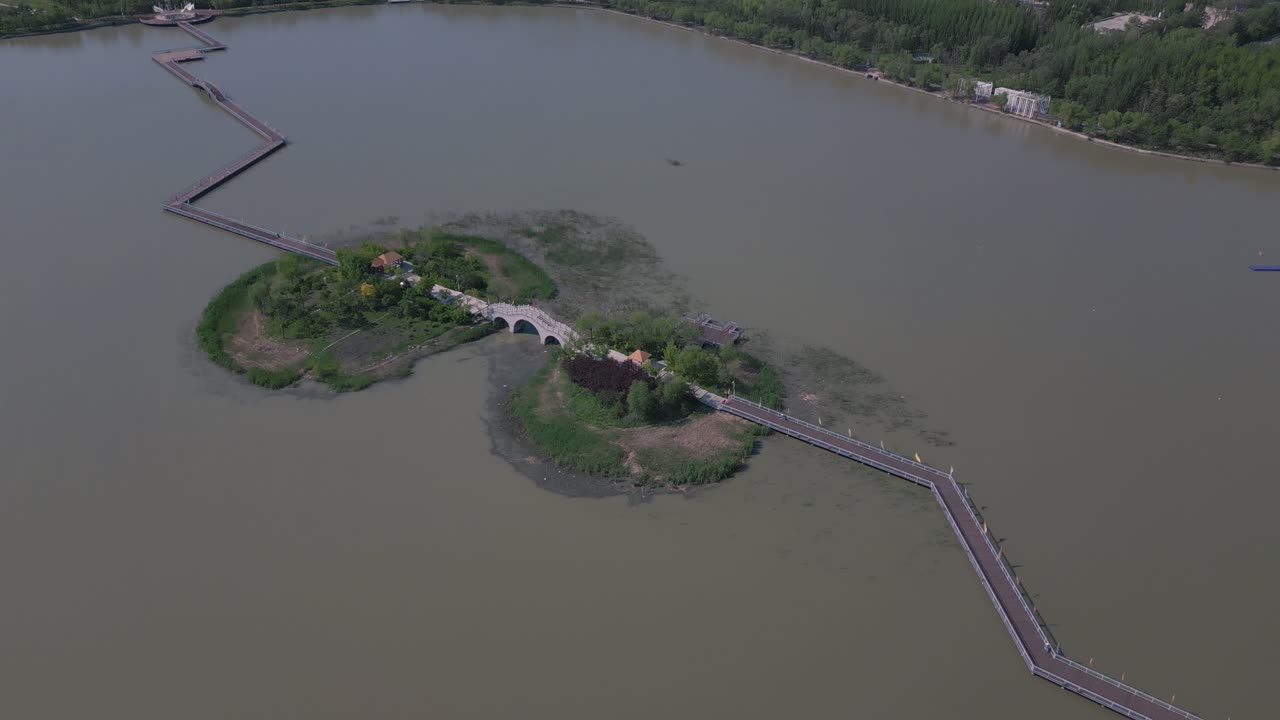 Stunning drone reveal footage of bridge on an island in the middle of a lake, and then panning to show a beautiful cityscape with a cell tower in the background in Daqing, China.