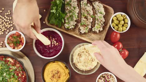 israeli cuisine. shakshuka in pan decorated with parsley, forshmak and hummus on table, eating pita with sauces. national jewish dishes top view. eggs fried in tomato sauce, middle eastern culture