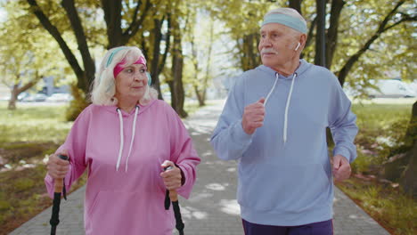 cheerful senior old couple grandfather, grandmother training nordic walking, running in summer park