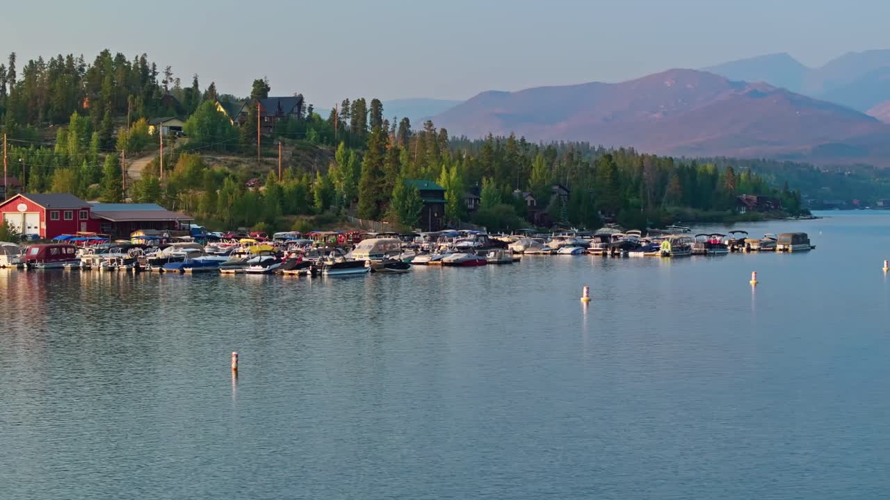 Drone orbit harbor marina surrounded by pine trees and mountain slopes at Grand Lake Colorado at golden hour
