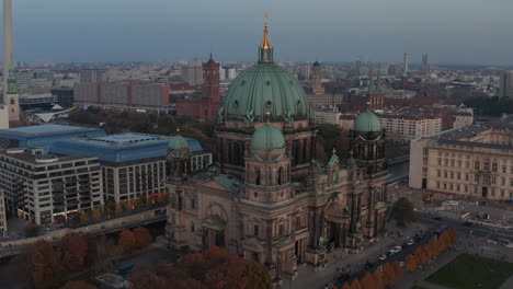 Orbit-shot-around-Berlin-cathedral,-valuable-historic-landmark-at-dusk.-City-in-background.-Berlin,-Germany