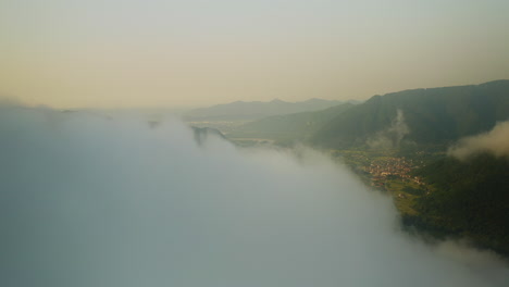 Aerial-reveal-shot-of-small-city-located-beside-Fiume-Piave-River-in-Northern-Italy-surrounded-by-Dolomite-Mountains-during-dusk